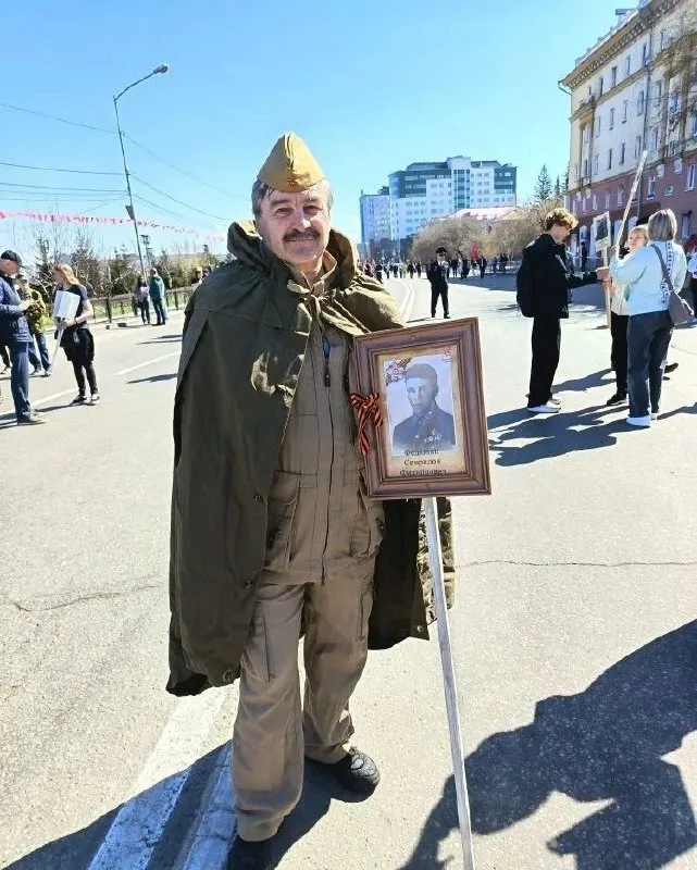 Максим Иванович несёт портрет деда Спиридона Филипповича Федюнина — солдата, пропавшего под Ржевом. Рядом его сёстры с портретом отца, призванного из Иркутска.